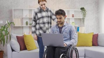 portion une désactivée homme dans une fauteuil roulant. désactivée homme travail avec portable est en difficulté et le sien petite amie est portion lui. video