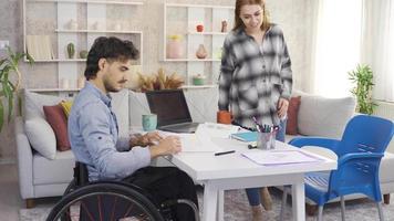 il ragazza aiuta e supporti il Disabilitato gioventù chi ha difficoltà nel studiando. Disabilitato maschio alunno e il suo fidanzata studia insieme a casa. utilizzando un' sedia a rotelle. video