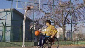 Desativado homem dentro cadeira de rodas comovente em basquetebol tribunal. cadeira de rodas basquetebol jogador jovem homem Treinamento ao ar livre em a tribunal. video