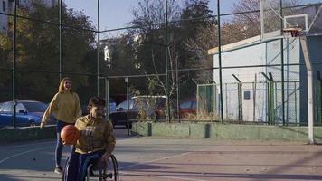 contento Disabilitato uomo giocando pallacanestro con il suo fidanzata all'aperto su il pallacanestro Tribunale. Disabilitato giovane uomo giocando pallacanestro con il suo fidanzata siamo contento e gioire. video