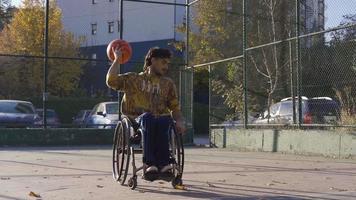Disabled young man in a wheelchair playing basketball outdoors. Disabled man playing basketball in wheelchair outdoors. video