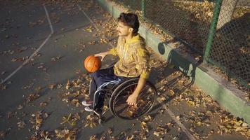 determinado discapacitado adolescente jugando baloncesto al aire libre en lento movimiento. discapacitado baloncesto jugador joven hombre enfocado en jugando baloncesto en lento movimiento. video