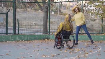 joven hombre en silla de ruedas jugando baloncesto en lento movimiento. discapacitado adolescente y su Novia jugando baloncesto al aire libre en lento movimiento. video