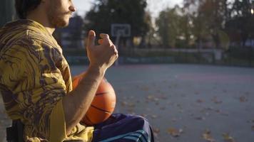 joven hombre en un silla de ruedas en el baloncesto corte. lento movimiento. seguro de sí mismo discapacitado adolescente jugando baloncesto al aire libre en lento movimiento. video