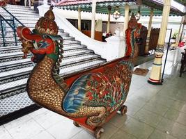A dragon shaped wooden statue is on the stairs in front of a staircase photo