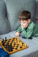 Boys play wooden chess lying on a gray sofa. photo