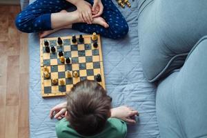 Boys playing wooden chess lying on a gray sofa, top view photo