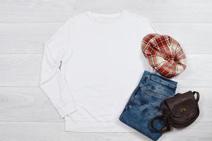 blanco camisa de entrenamiento Bosquejo. modelo blanco camisa parte superior ver en blanco de madera antecedentes. invierno atuendo en madera piso. mujer Moda ropa. primavera Mira de hoy. hembra vaqueros, sombrero, bolso accesorios foto