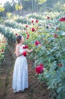 Young Asian woman wearing a white dress poses with a rose in rose garden photo