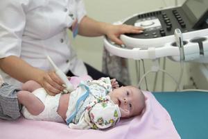 el médico hace un ultrasonido escanear para un recién nacido bebe medico examen de un bebé por ultrasonido equipo foto