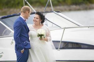The fat bride and groom stand near the yacht and talk to each other. photo