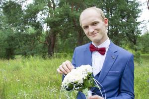 retrato de el novio de europeo apariencia en un azul Boda traje con un ramo de flores de flores foto