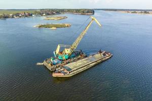 aerial view on crane extracts minerals from bottom onto huge barge in middle of lake or sea photo