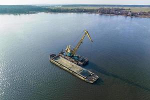 aerial view on crane extracts minerals from bottom onto huge barge in middle of lake or sea photo