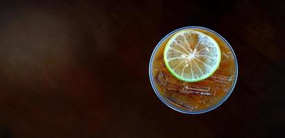 Top view of iced lemon tea on dark brown wooden background. Cup or plastic glass cool lime coffee on wood table with copy space. Refreshment drinking photo