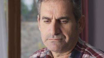 Unhappy man looking out the window. Unhappy and depressed mature man looks out the window and into the camera. video