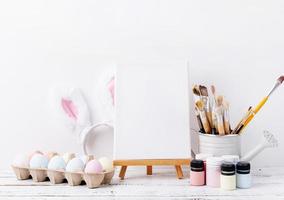 Pastel colored Easter eggs and mimosa flowers with blank white frame for mockup design, front view on white brick wall background photo
