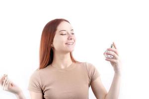 Happy young woman using perfume, holding glass bottle isolated on white background photo