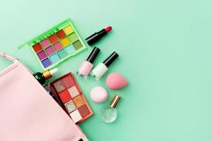 Bright summer eyeshadow palette and makeup products in pink cosmetic bag on green background photo