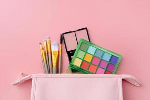 Bright summer eyeshadow palette and makeup products in pink cosmetic bag on pink background photo