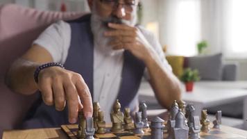 riflessivo uomo giocando scacchi e pensiero di il suo si sposta. maturo uomo giocando scacchi solo a un' tavolo a casa. video