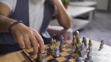 mature homme en jouant échecs seul à une table à maison. intelligent homme en jouant échecs seul à maison, élaborer des stratégies. video