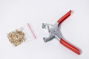 Hand punch for eyelets with a set of golden eyelets in a zip bag on a white background. Hand tool for installing eyelets in the form of forceps or pliers with eyelets on a horizontal background photo