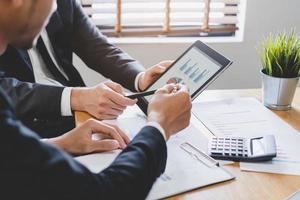 Business meeting, two caucasian, asian group man use tablet brainstorm analyzing on graph data of cost plan or document, paperwork and discussing in board room on table. People working conference room photo