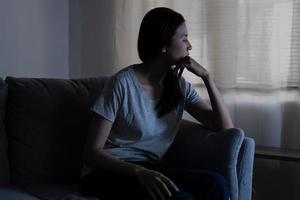 Mental health, depressed sad asian young woman, girl sitting on sofa, couch, expression to face difficulty, failure and exhausted. Thoughtful worried suffering depression feeling lonely, alone at home photo