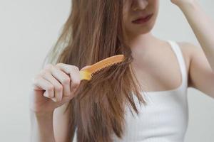 Damaged Hair, frustrated asian young woman, girl hand in holding brush splitting ends messy while combing hair, unbrushed dry long hair. Health care beauty, portrait isolated on white background. photo