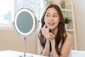 Fresh, nice healthy skin, beautiful of asian young woman, girl looking at mirror, touching her face with before make up cosmetic routine at home. Female look with natural fashion style, Facial Beauty. photo