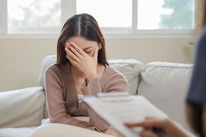 psicología, depresión. triste, sufrimiento asiático joven mujer consultante con psicólogo, psiquiatra mientras paciente asesoramiento mental con médico mujer tomando notas a clínica. alentador, terapia. foto