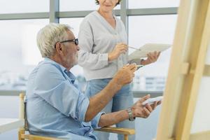 Happy older husband, wife senior couple elderly family, caucasian mature, adult and retirement having pleasure together and painting picture on canvas at home. Freetime, relaxed lifestyle of people. photo