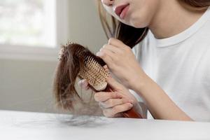 dañado cabello, frustrado asiático joven mujer, niña mano en participación cepillo terrible termina sucio mientras peinada cabello, sin cepillar seco largo cabello. salud cuidado belleza, retrato aislado en blanco antecedentes. foto