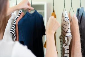 elección de ropa, nada a vestir asiático joven mujer, niña mano en elegir vestido, atuendo en percha en guardarropa en habitación armario a hogar. decidiendo qué a poner en cuales uno. foto