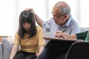 Asian father, grandfather and mental health patient, girl child, granddaughter have appointment visit doctor at clinic, consulting psychiatrist, treatment by therapy. Health care, check up medical. photo