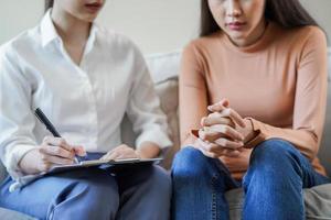 psicología, depresión. triste, sufrimiento asiático joven mujer consultante con psicólogo, psiquiatra mientras paciente asesoramiento mental con médico mujer tomando notas a clínica. alentador, terapia. foto