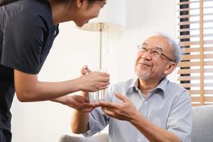 asiático joven mujer cuidador, cuidador secundario anciano, Envejecido paciente a hogar, Bebiendo agua después tomar medicamento, cura o tratamiento enfermedad de abuela después Jubilación, ayuda apoyo. foto