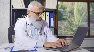maduro médico homem trabalho dentro dele privado clínica. maduro médico homem trabalhando em dele computador portátil. video
