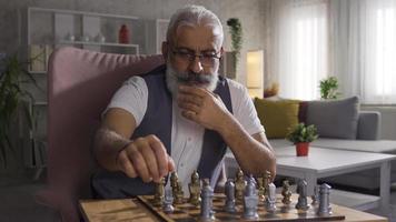 Senior Man Playing Chess At Home Alone. The man alone at home is playing a game of chess. video