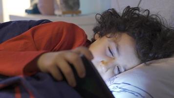 téléphone intoxiqué enfant est sieste et continue à Regardez à le téléphone. le Jeune homme en jouant le téléphone dans le sien lit à nuit obtient somnolent et continue à Regardez à le téléphone. video