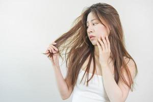 Damaged Hair, frustrated asian young woman, girl hand in holding splitting ends, messy unbrushed dry hair with face shock, long disheveled hair, health care of beauty. Portrait isolated on background. photo