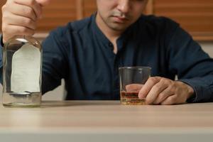 alcoholismo, Deprimido asiático joven hombre torrencial, participación botella whisky dentro el vaso, Bebiendo alcohol bebida a noche. tratamiento de alcohólico adiccion, sufrir abuso problema alcoholismo concepto. foto