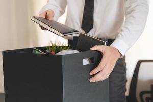 Unemployed, quite job. Desperate caucasian young businessman resigning from company, hand holding stuffs into the cardboard, packing belongings, layoff or changing work. Resignation,employment concept photo