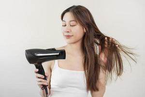 Hair Dryer, beautiful happy, asian young woman, girl hand in using, holding hairdryer to dry, blowing blonde long straight after shower at home. Hairdressing, hair treatment isolated on background. photo