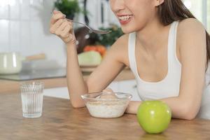 Pretty girl, happy meal eating healthy breakfast in morning, asian young woman having cereals, granola with fresh dairy milk in bowl  in kitchen. Dieting, vegetarian food people concept. photo