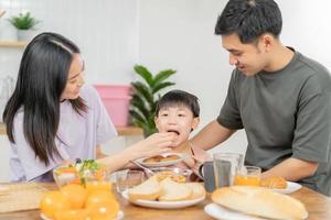 Happy refreshment family breakfast in morning, asian young parent father, mother and little cute boy, child having meal in kitchen eating together at home. Cheerful, enjoy cooking people. photo