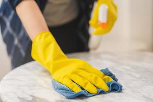 Cleaning hygiene, close up hand of maid, waitress woman wearing yellow protective gloves while cleaning on wood table, use blue rag wiping to dust and spray in restaurant. Housekeeping cleanup,cleaner photo