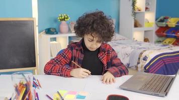 bem sucedido Garoto desenha às mesa dentro crianças sala. a criança desenha uma criativo cenário usando dele imaginação. video