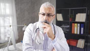 el pensativo mayor médico tiene muchos problemas en su mente. mayor médico es pensativo y pensamiento, jugando con su barba. video